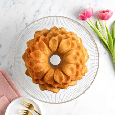 Overhead image of plain Blossom Bundt cake on clear cake stand with pink flowers and plate