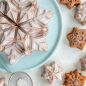 Baked and glazed snowflake cake on a blue platter, snowflake cakelets on the surface, dusted with powdered sugar