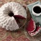 Baked red velvet Stained Glass Bundt cake with white glaze on serving plate, slices cut from cake on plate with fork, cup of coffee