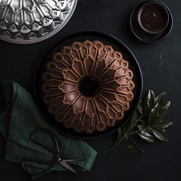 Baked chocolate Stained Glass Bundt cake on serving plate, pan beside cake, chocolate in dish