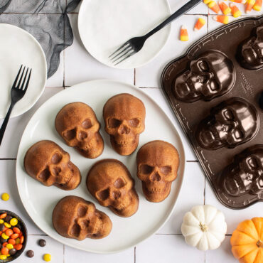 Skull cakelets on plate against tile backdrop, pan next to plate