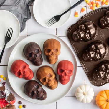 Multi flavor skull cakelets on plate against tile backdrop, pan next to plate