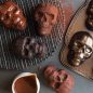 Baked chocolate skull cakeletes on cooling rack, chocolate glaze and pan in background