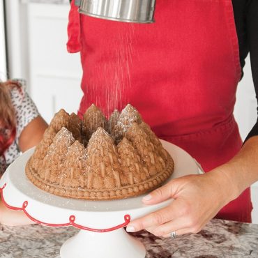 Baked Pine Forest Bundt cake with woman dusting powdered sugar on cake in kitchen scene