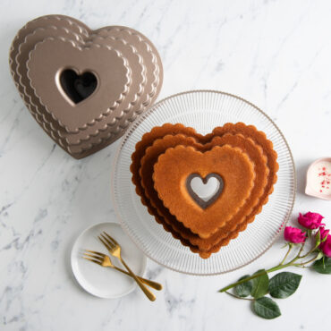 Plain Tiered Heart Bundt on clear cake stand surrounded by roses and pan, overhead