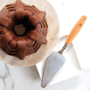 Golden bundt cake on white square plate with Nordic Ware stainless steel cake server beside it