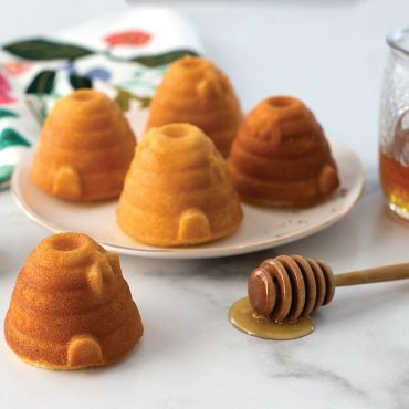 Baked almond beehive cakelets on plate, one cake on surface with honey dipper