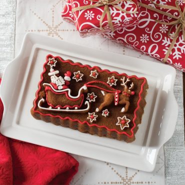 Baked gingerbread loaf with piped red and white frosting details, on serving plate
