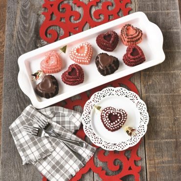 Top view heart baked cakes with various decorations and glazes on serving plate, one cake on plate with paper gold arrow through it