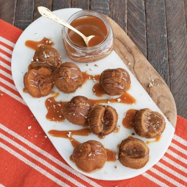 Baked apple spice cakes with caramel glaze on serving tray, jar of caramel glaze and spoon