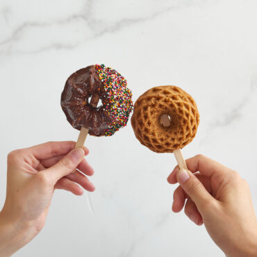 Two hands holding Geo Bundtlettes on a stick, one glazed and decorated