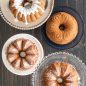 Top view of baked vanilla Bundt cakes, all four designs, one white glaze, one plain, one dusted with powdered sugar, one with glaze on whole cake