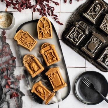 Tombstone cakelets on black plate with Pan, white tile backdrop, dry ice fog swirling around cakelets