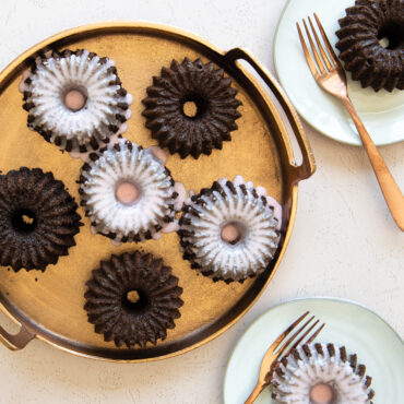 Baked Brilliance Bundtlettes on gold surface with chocolate cake and white glaze