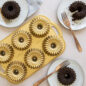 Baked Brilliance Bundtlettes on white surface with chocolate cake and pan