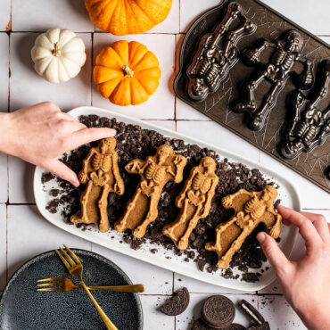 Spooky Skeleton Cakes on crumbled cookies, hands picking up cakes