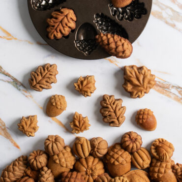 Nordic Ware aluminum Woodland cakelet pan with baked golden cakelets shaped like leaves, acorns, and pinecones