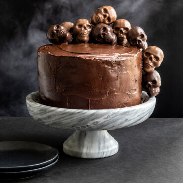 Small skull-shaped cakelets with white frosting and colorful sprinkles made using Nordic Ware Skull Bites pan