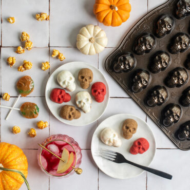 Various skull bites on plates against white tile backdrop, pan and pumpkins next to plate with candy
