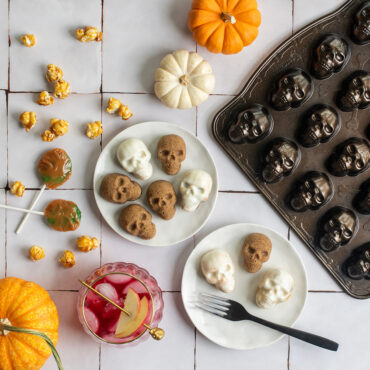 Various skull bites on plates against white tile backdrop, pan and pumpkins next to plate with candy