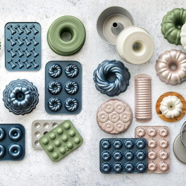 Collection of Nordic Ware aluminum baking pans in various shapes including bundt, loaf, and specialty molds with natural silver finish