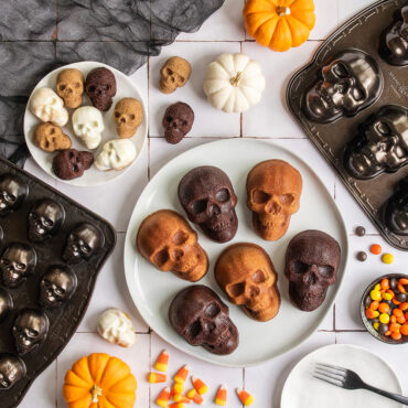 Skull bites and cakelets scene on plates against white tile backdrop, pans and pumpkins next to plate with candy