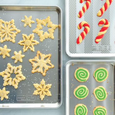 Assorted holiday cookies including stars, trees, and decorated shapes baked on Nordic Ware aluminum half sheet pans
