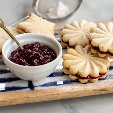 Stamped cookie sandwiches filled with berry jam, dusted with powdered sugar