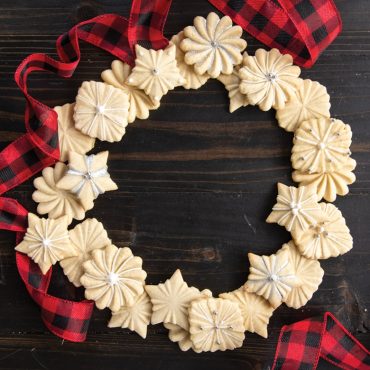 Decorated baked pleated cookies in a wreath shape on surface with holiday ribbon around cookies