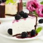 vanilla cheesecake slice with chocolate crumb crust, blackberry garnish on plate