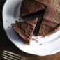 Chocolate round cake on cake platter, one cut piece