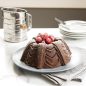 Baked chocolate Marquee Bundt with raspberries in the middle dusted with powdered sugar, plates in background.