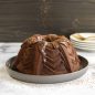 Baked chocolate Marquee Bundt with espresso glaze, being dusted with cocoa powder