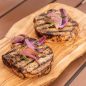 grilled pork chops on wooden board topped with onions and herbs