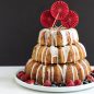 3 tiered baked cakes with glaze, surrounded by fresh fruit, on platter