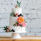 three tiered white frosted wedding cake with roses,peonies, greens decorations cake on cake stand