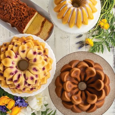 Top view of baked Lotus Bundt, Wildflower Loaf, Magnolia Bundt, Blossom Bundt cakes on serving plates with flowers