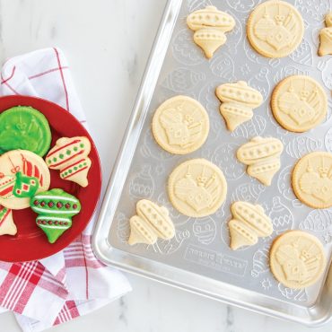 Baked Yuletide design cookies and cookie cutouts on ornament embossed half sheet.