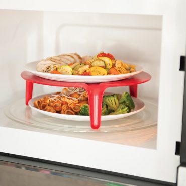 Plate of pasta and broccoli under raised red stand, plate of sliced chicken and sliced summer squash on top tier of stand, in microwave