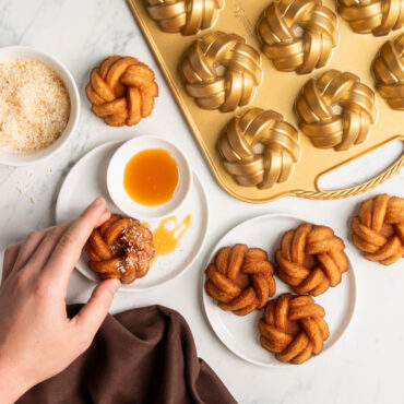 hand grabbing mini bundts on white serving plates with caramel drizzle and coconut flakes made with Nordic Ware aluminum braided mini bundt pan
