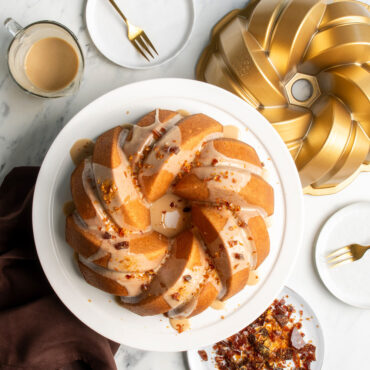 Golden glazed bundt cake with braided rope design next to Nordic Ware aluminum bundt pan and serving plate
