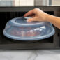 Hand placing cover on top of plate of food in microwave