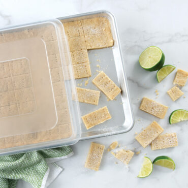 Nordic Ware aluminum half sheet pan with clear lid, containing golden baked bars cut into squares