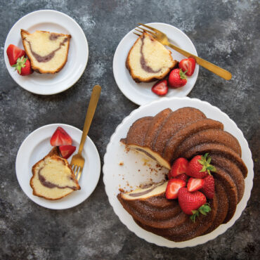 Sliced bundt cake with swirled pattern from Nordic Ware Swirl Bundt pan, dusted with powdered sugar and topped with fresh strawberries