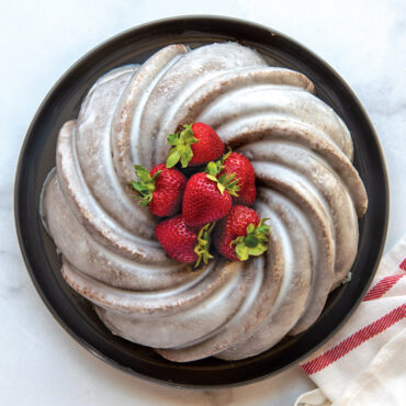 Golden swirl bundt cake with white glaze and fresh strawberries, baked in Nordic Ware aluminum bundt pan