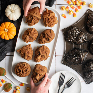 Monster Mask Cakelets on plate next to pan on tile backdrop, assorted Halloween candy spread throughout