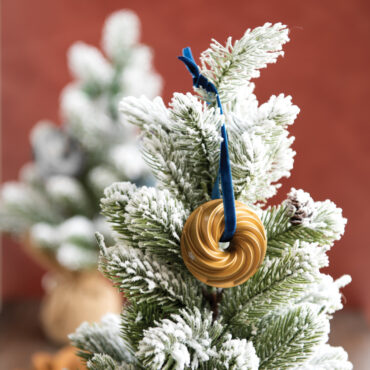 Nordic Ware gold-colored Heritage Bundt pan ornament hanging on white Christmas tree branch