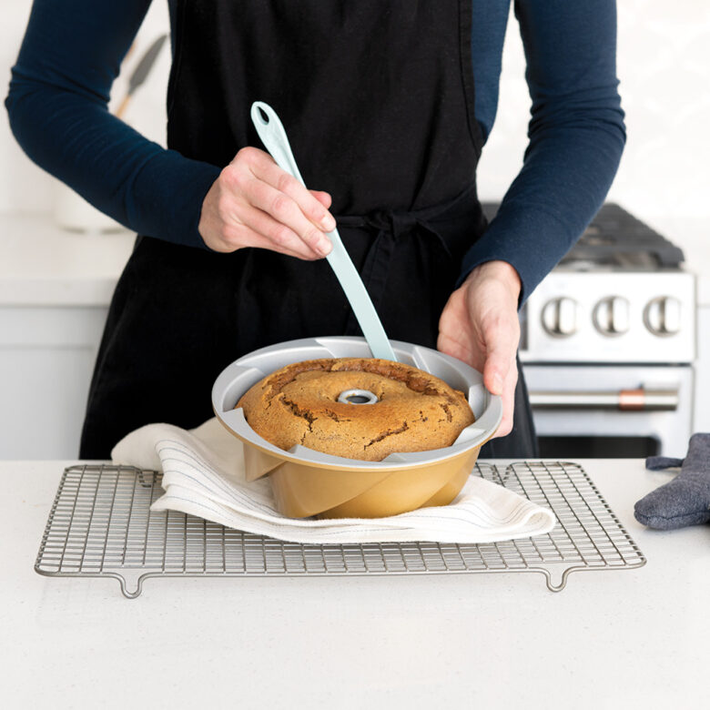  Image of a woman inverting a Bundt cake onto a cooling rack in a kitchen.