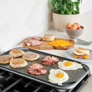 A side image of the griddle on the stovetop making breakfast sandwiches on the smooth side of the reversible griddle