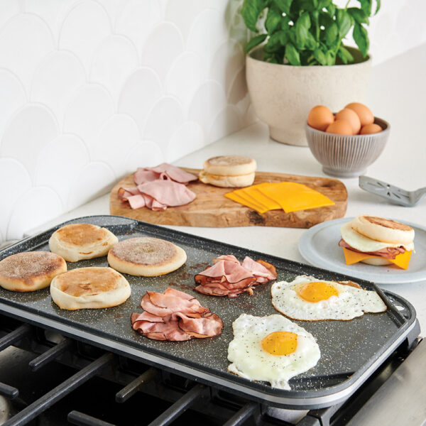 A side image of the griddle on the stovetop making breakfast sandwiches on the smooth side of the reversible griddle